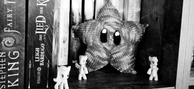 Ein gestrickter Stern mit süße Augen im Bücherregal.